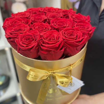 Round gold hat box filled with tightly packed red roses and tied with a yellow satin ribbon