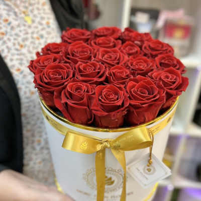 Round white hat box filled with tightly packed red roses and tied with a gold ribbon