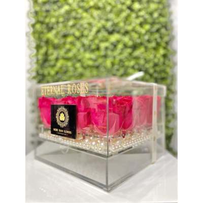 Hot pink roses in a clear acrylic box with pearls at the base against a green wall