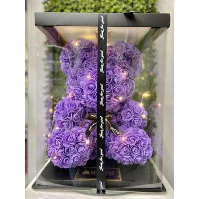 Purple artificial rose teddy bear with string lights in a clear gift box