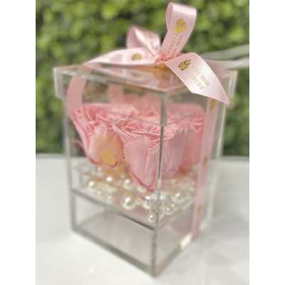 Pink roses arranged in a clear acrylic box with pearl beads and a pink ribbon bow