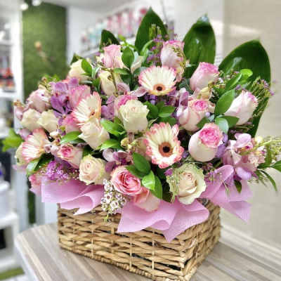 Low basket arrangement of pink gerbera daisies and roses with white accent flowers
