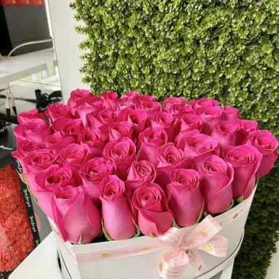 Round white hatbox filled with tightly packed bright pink roses and a pink ribbon bow