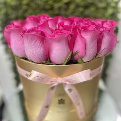 Bright pink roses arranged in a round gold hatbox with a tied pink ribbon.