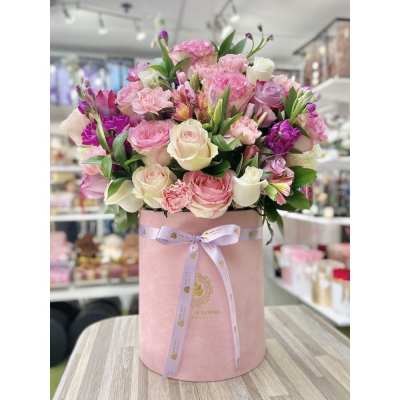 Pink and cream rose and carnation arrangement in a tall pink hatbox with ribbon on a wooden table