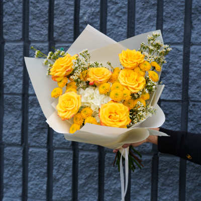 Bouquet of yellow roses and small white flowers wrapped in white paper