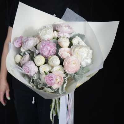 Handheld bouquet of pale pink and white ranunculus wrapped in white paper
