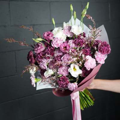 Handheld bouquet of pink, purple, and white flowers wrapped in paper