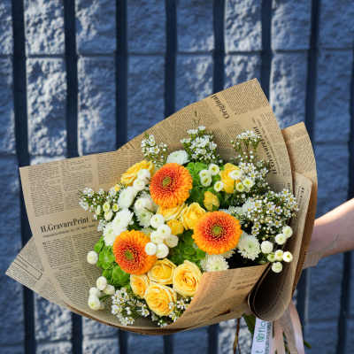 Bouquet of yellow roses and orange gerbera daisies wrapped in newspaper-style paper