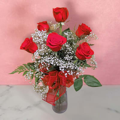 Red roses in a glass vase with baby's breath and a red ribbon