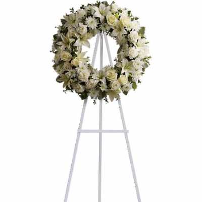 White floral wreath on a tall white easel stand.