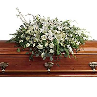 White lilies and roses casket spray arranged on top of a polished wooden coffin