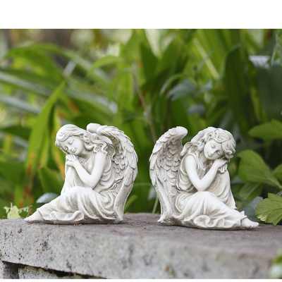 Pair of white sleeping angel figurines on a stone ledge outdoors