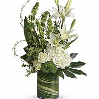 Tall white and green arrangement with lilies, hydrangea, roses, and bells of Ireland in a glass cylinder vase.