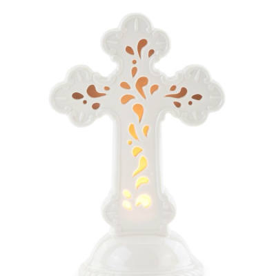 White ceramic cross with cutout pattern glowing with warm light