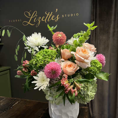 Mixed bouquet of peach roses, pink dahlias, and white chrysanthemums in a white vase
