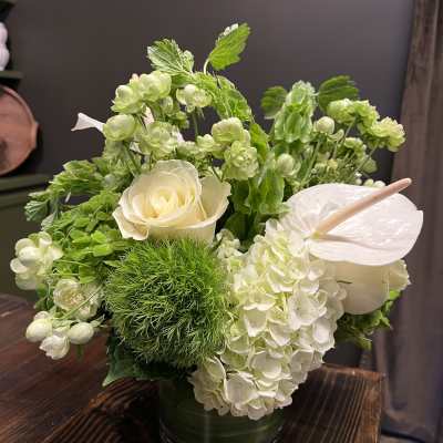 White roses and hydrangeas in a green vase with anthurium and green blooms