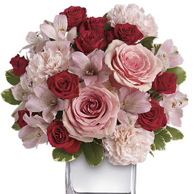 Compact arrangement of pink and red flowers in a clear glass cube vase