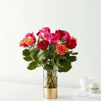 Tall glass vase with pink, red, and orange roses on a white surface