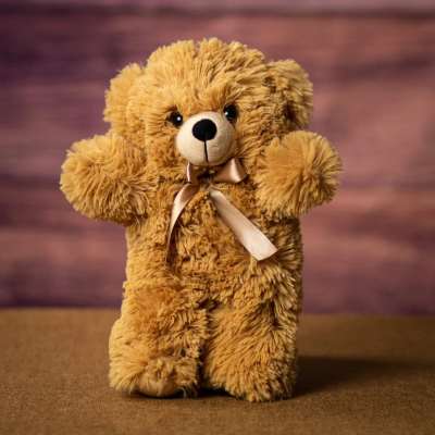 Fluffy light brown teddy bear plush with a satin bow on a brown surface.