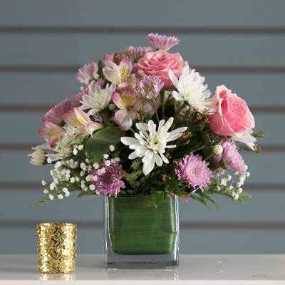 Pink and white mixed bouquet in a square glass vase beside a gold candle holder
