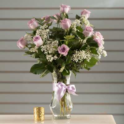 Lavender roses arranged in a clear glass vase with a satin ribbon.