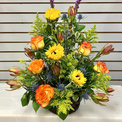 Basket arrangement with orange roses, yellow sunflowers, and blue thistle