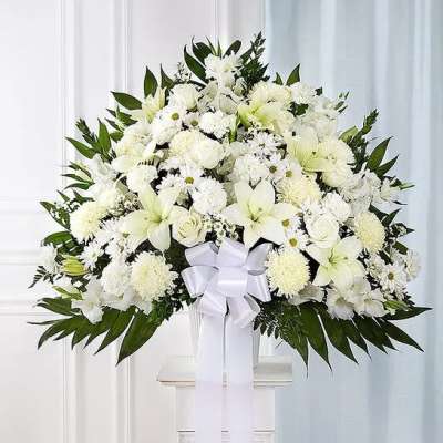 Large white floral arrangement with lilies, roses, and a white bow in a vase.