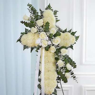 Standing cross of white flowers with white roses and ribbon on an easel