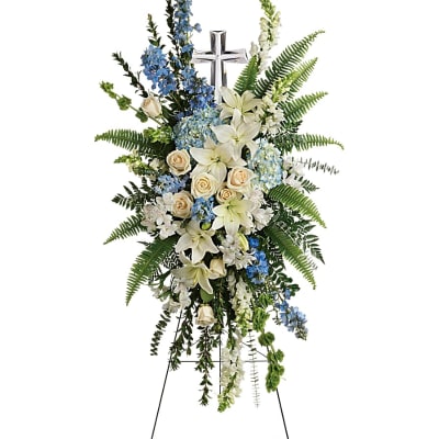 Tall blue and white standing spray with lilies and roses on an easel with a silver cross