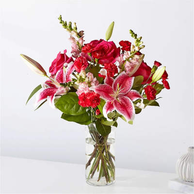 Pink lilies, red roses, and red carnations arranged in a clear glass vase with water