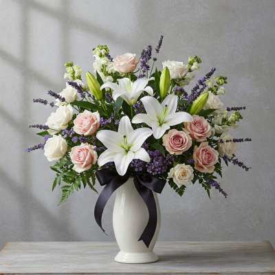 White lilies and pink and white roses in a white vase with a black ribbon