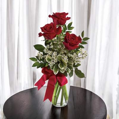 Red roses arranged in a clear glass vase with a red ribbon