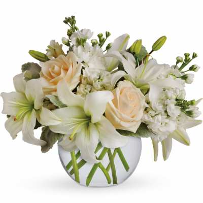 Low arrangement of white lilies and cream roses in a round glass vase