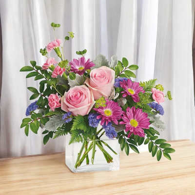 Pink roses and magenta daisies arranged in a clear glass vase.