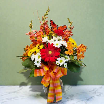 Colorful mixed flower arrangement in a vase with a plaid ribbon and butterfly pick