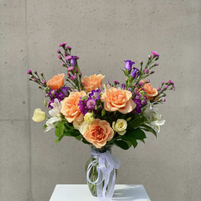 Peach and purple bouquet in a clear glass vase with a ribbon