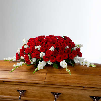 Red rose casket spray with white accent flowers on a wooden casket
