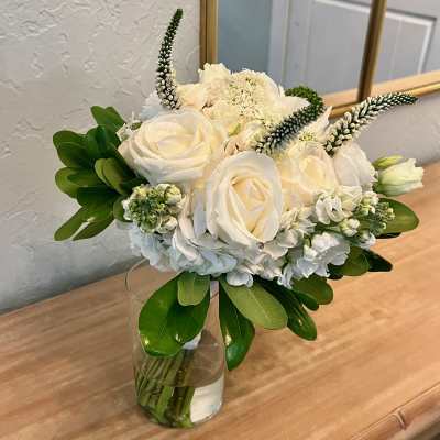 Compact white rose and hydrangea arrangement with greenery in a clear glass vase