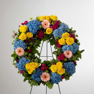Circular wreath of blue hydrangeas, yellow roses, pink gerberas, and magenta spray roses