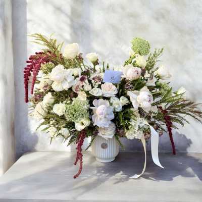 White and blush floral arrangement in a ribbed vase with trailing burgundy accents