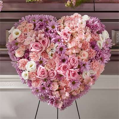 Heart-shaped standing arrangement of pink and lavender roses, carnations, and daisies.