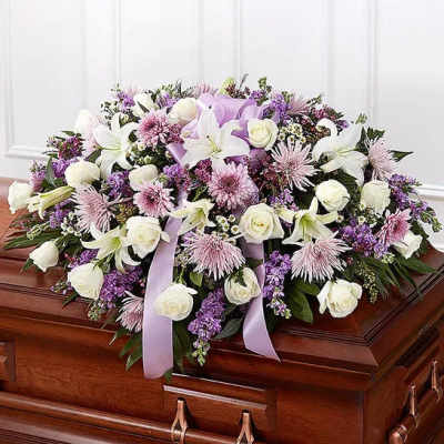 Lavender and white casket spray with roses, lilies, and mums on a wooden casket
