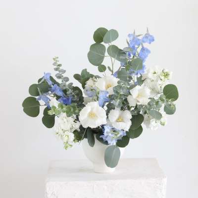 Blue and white flowers arranged in a white vase with round eucalyptus leaves