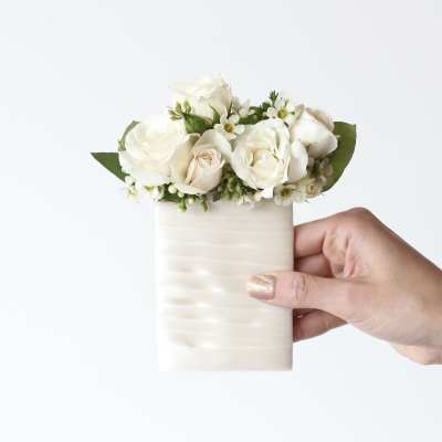 White rose bouquet in a small ivory vase held in a hand