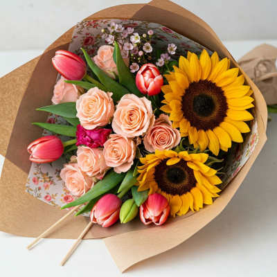 Bouquet of peach roses, red tulips, and sunflowers wrapped in brown paper