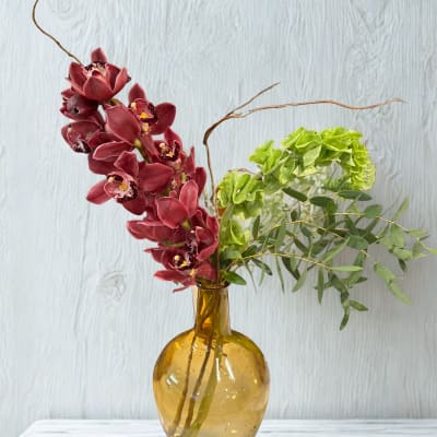 Burgundy orchids and green foliage in an amber glass vase