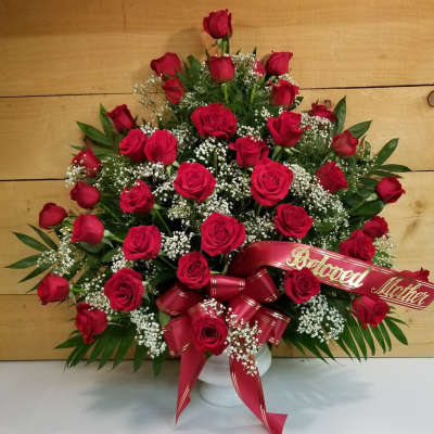 Red roses arranged in a white vase with a red ribbon