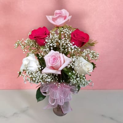 Bouquet of pink, red, and white roses in a glass vase with a pink ribbon