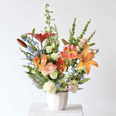 Mixed bouquet of lilies, roses, and blue flowers in a white vase